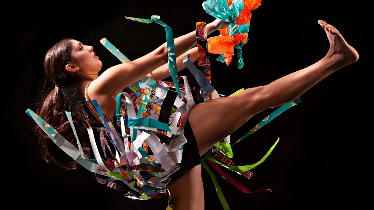 A dancer throwing their leg in the air, surrounded by colorful ribbons of fabric